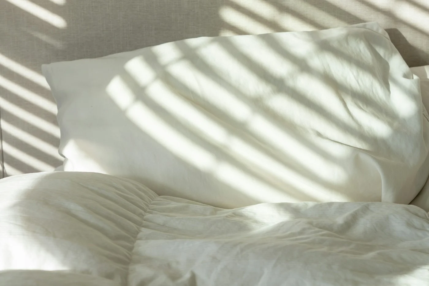White bed linens with soft sunlight and striped shadows.