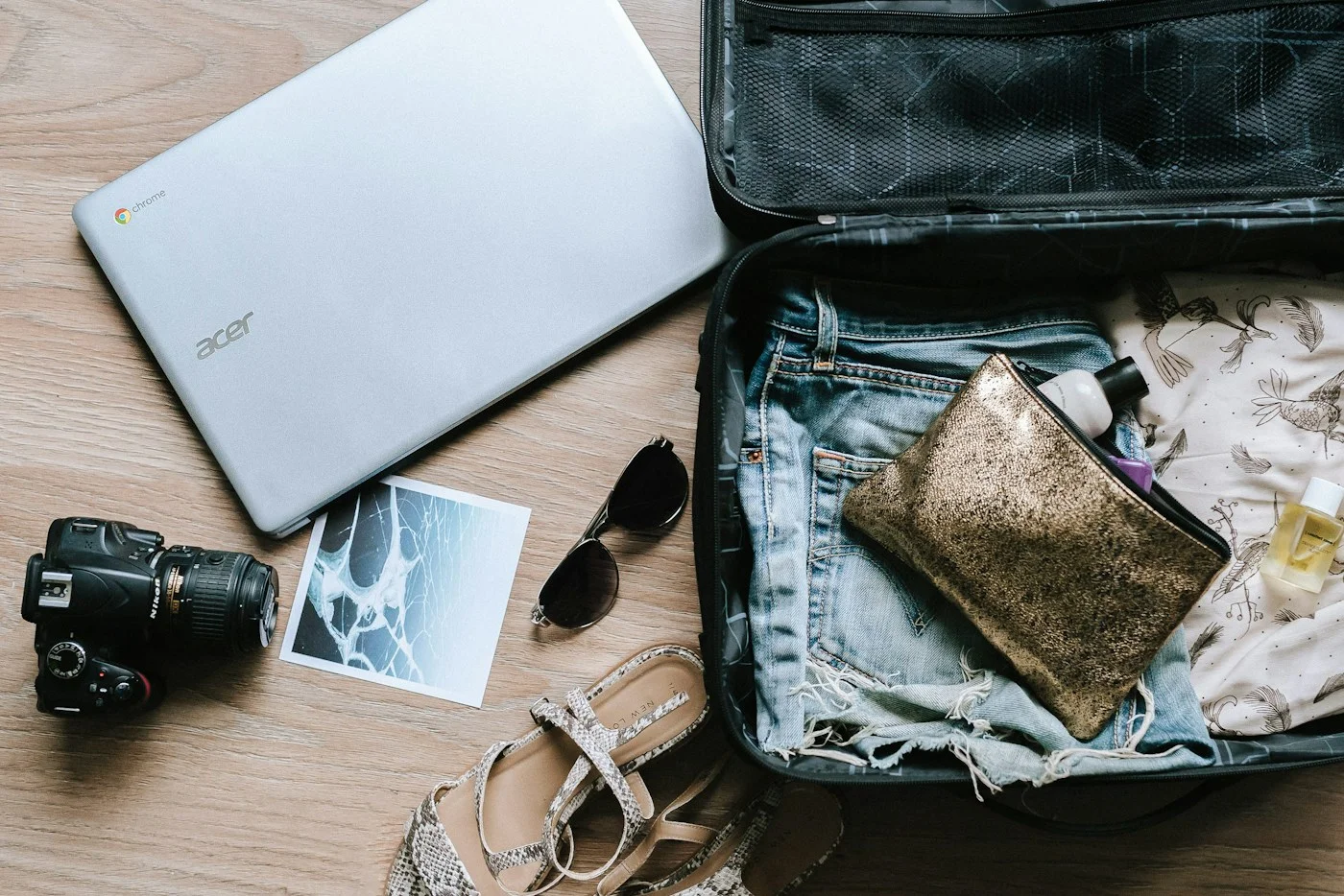 An open suitcase with folded clothing, a travel wallet, and a camera beside it.