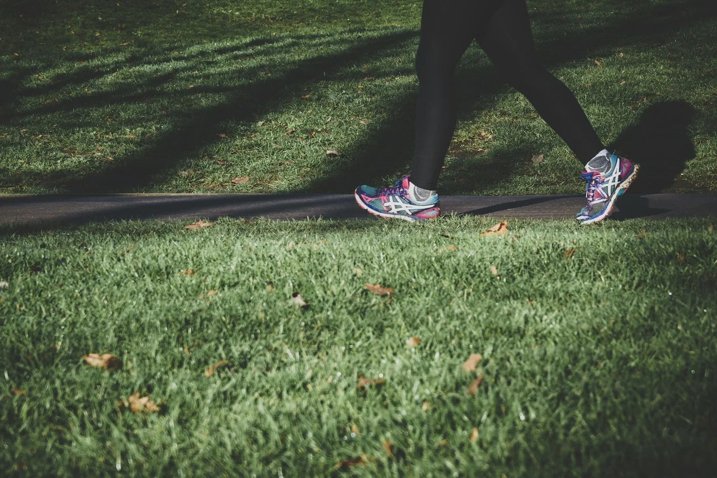 A person wearing walking shoes on a sunlit path beside grass.
