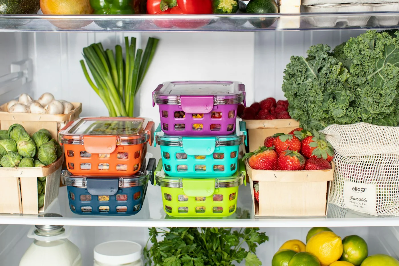 Colorful lidded lunch containers arranged with fresh produce in a refrigerator.