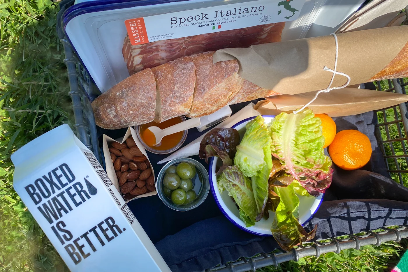 Bread, fruit, salad, and drinks packed for a picnic on a blanket.