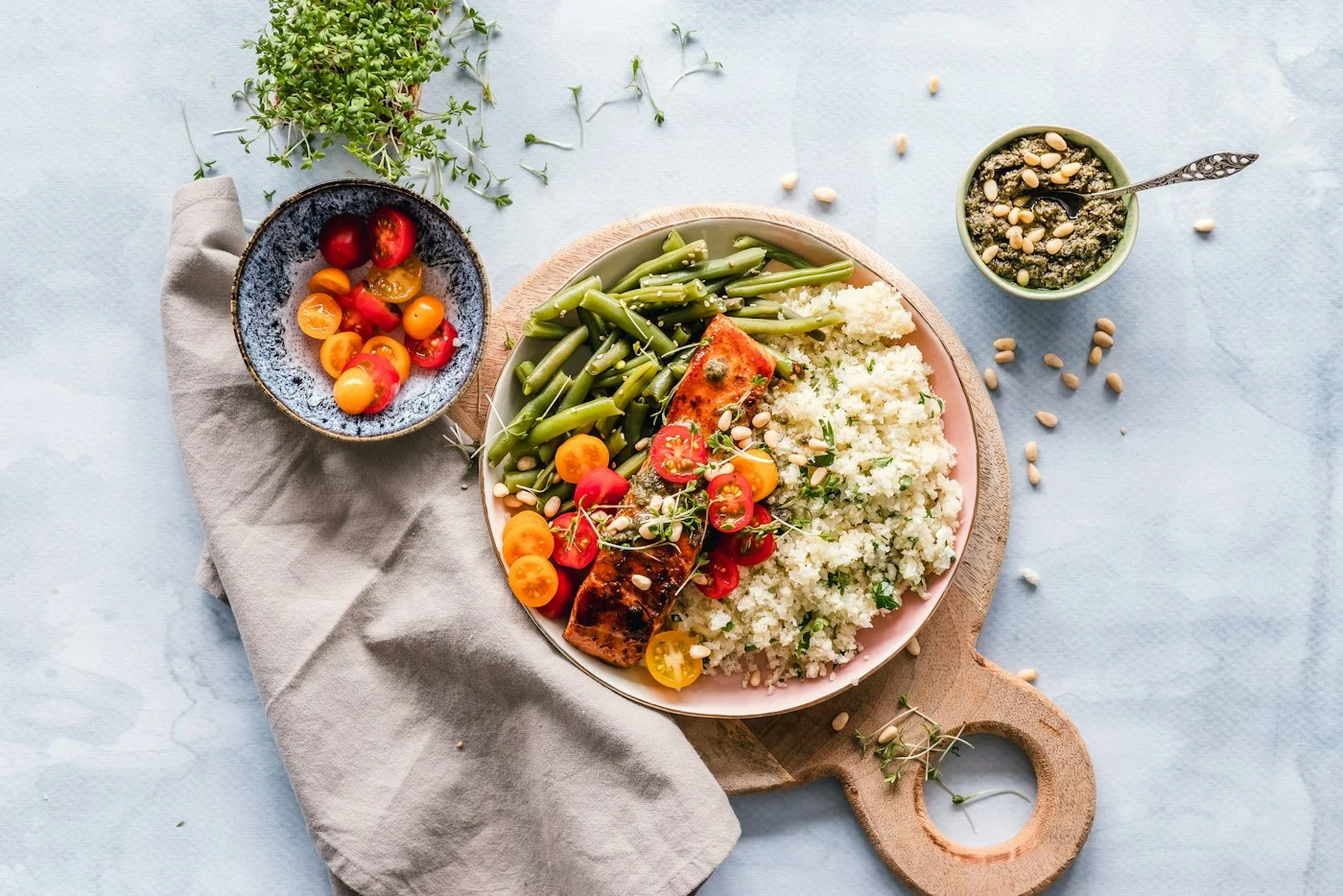 A bowl of grains and vegetables beside fruit and a wooden spoon.