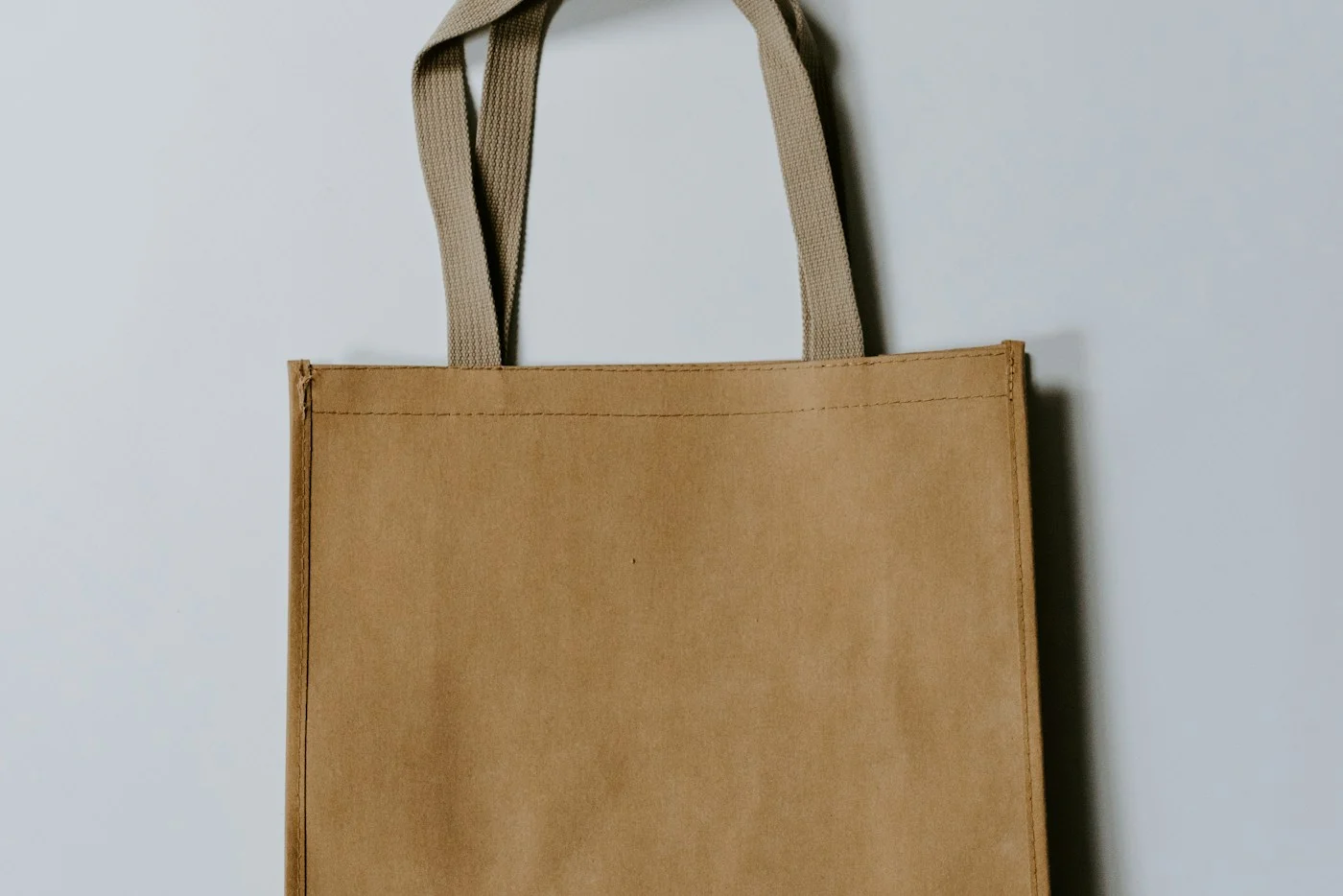 A simple brown canvas tote hanging against a light wall.